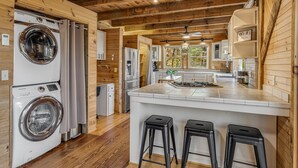 Une cuisine moderne avec des poutres en bois, un îlot central doté de tabourets de bar, un lave-linge encastré et une vue sur l’extérieur.