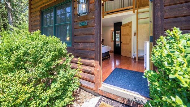 Una baita di legno con facciata in legno, una scala a vista per un piano superiore e un tappetino blu all'ingresso.