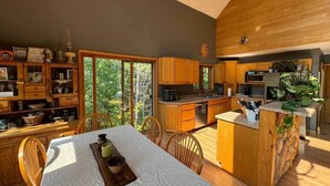 Una cocina moderna con armarios de madera, una zona de comedor con mesa y sillas, y ventanas amplias con vistas al exterior.