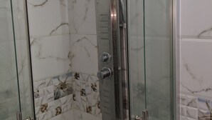 Une douche fermée par des parois en verre, dotée d’un pommeau de douche à main et d’un panneau de commande.