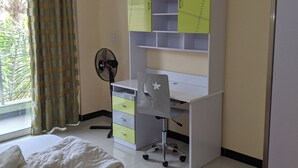 Une chambre à coucher comprenant un lit, un bureau avec des placards, une chaise et un ventilateur.