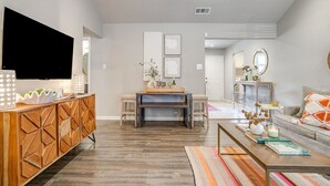 A modern living room with a wooden cabinet, a flat-screen TV, a dining area with a bench, and a sofa with a patterned throw. - Darling Fort Worth Getaway! Located near The Stockyards,Downtown & TCU (Westworth Village)
