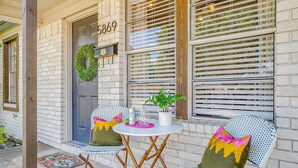 A brick house with a number 5869 on the door, two chairs with cushions, a small table with a plant, and a wreath on the door. - Darling Fort Worth Getaway! Located near The Stockyards,Downtown & TCU (Westworth Village)