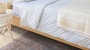 A neatly made bed with a checkered bedspread, a bedside lamp, and a framed picture on the wall.