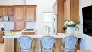A kitchen with wooden cabinets, a central island with bar stools, a stove, and a sink.