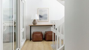 A narrow hallway with a wooden floor, white walls, a white railing, and a framed picture on the wall.