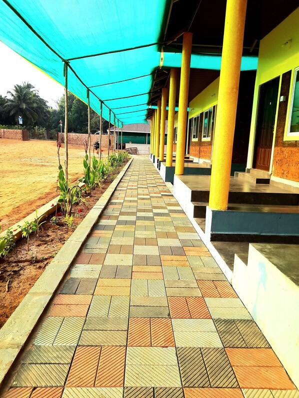 A covered walkway with patterned tiles, yellow pillars, and a brick wall in the background. - SEA SPRAY RESORT (Kumta)