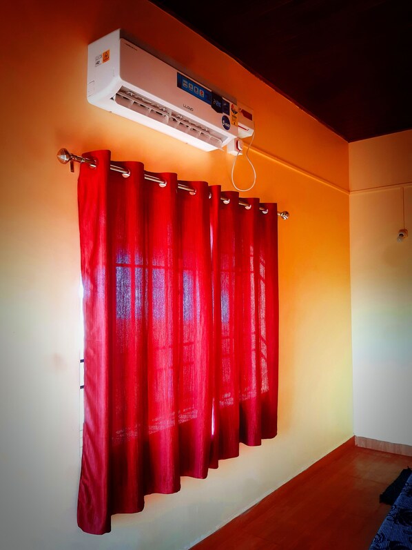 A room with a red curtain, a ceiling-mounted air conditioner, and a wooden floor.