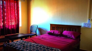 Een kamer met een bed, een stoel, een tafel en een raam met gordijnen.