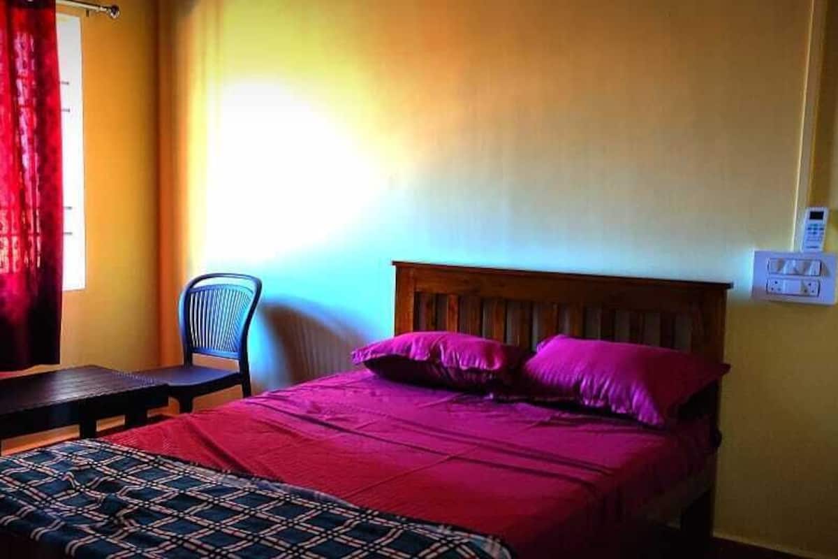 A room with a bed, a chair, a table, and a window with curtains.