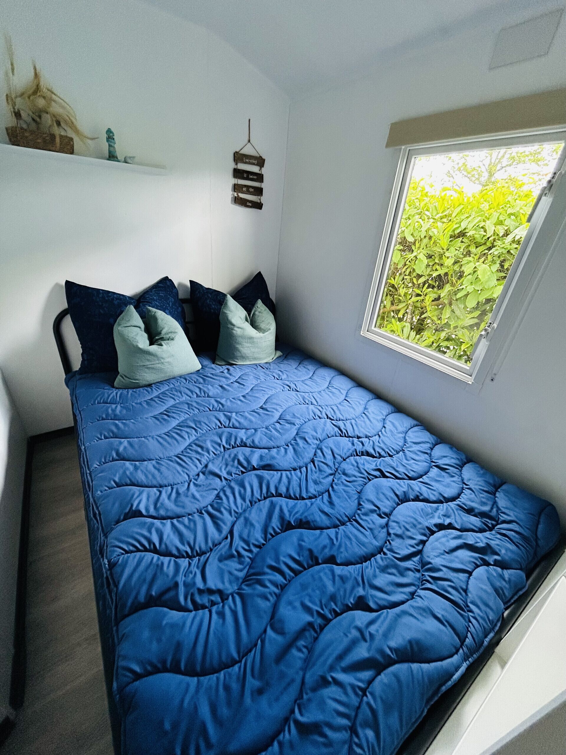 A bedroom with a bed, pillows, a hanging light fixture, and a window with a view of greenery.