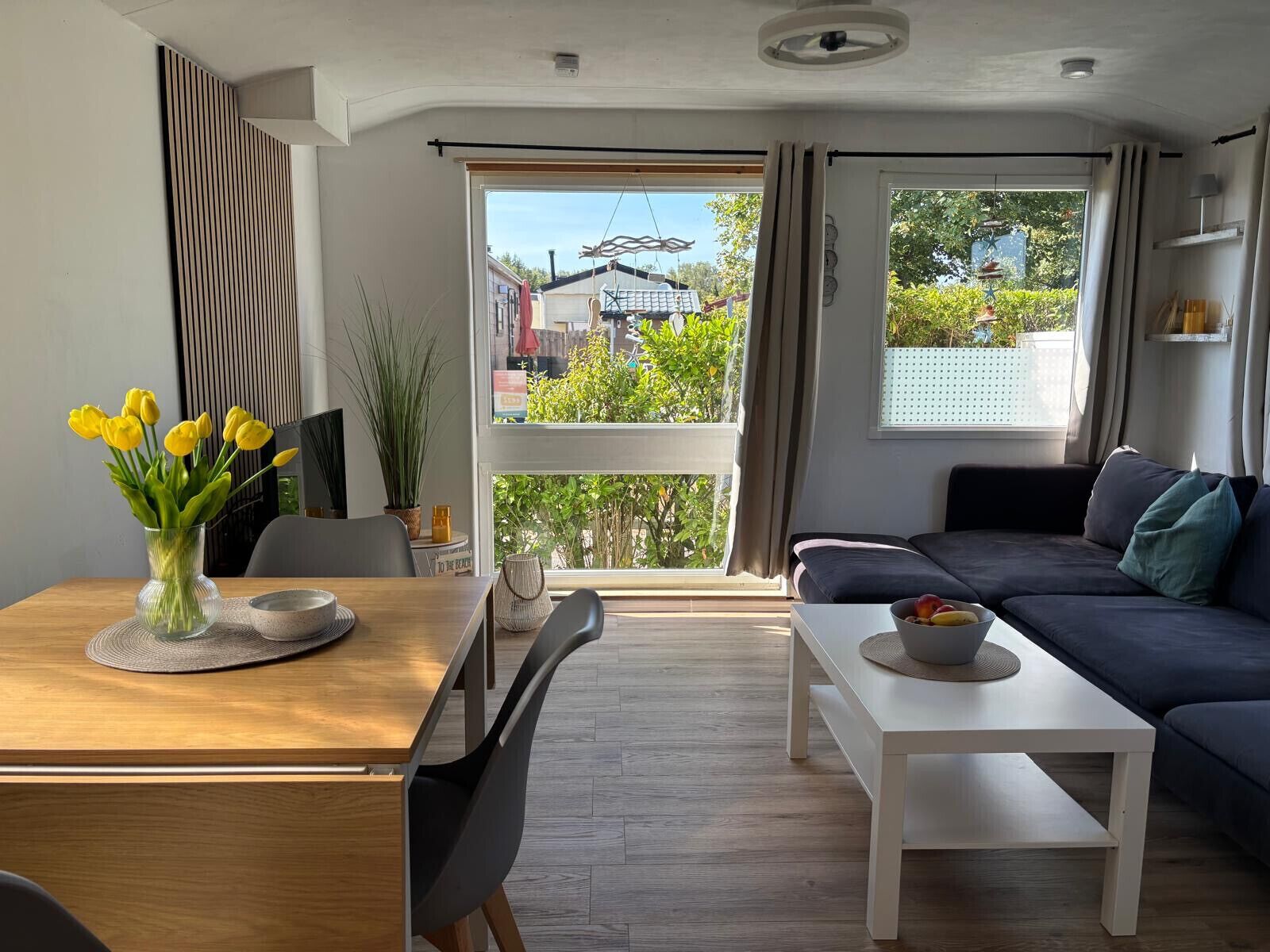Un salon moderne avec un canapé, une table à manger et des chaises, et une vue sur l’extérieur grâce à de grandes fenêtres.