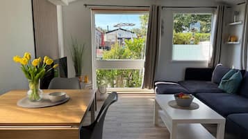 Un salon moderne avec un canapé, une table à manger et des chaises, et une vue sur l’extérieur grâce à de grandes fenêtres.