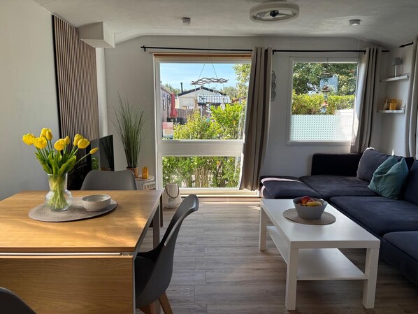 A modern living room with a sofa, a dining table with chairs, and a view of the outdoors through large windows. - RBR 511 - Beach Resort Kamperland (Kamperland)