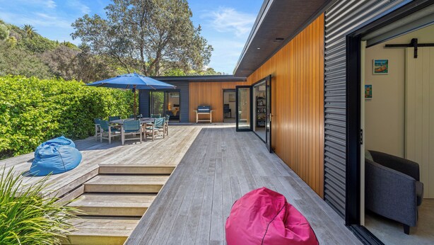A modern outdoor deck with wooden flooring, a dining area with chairs and a table, and a blue umbrella.
