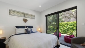 A bedroom with a large bed, a heart-shaped decoration on the wall, and a view of greenery through a sliding door.