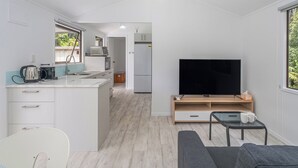 A modern, compact living space with a kitchen, dining area, and a seating area with a TV. - Rewa Rewa Retreat - Tairua Holiday Home (Tairua)