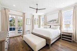 A bedroom with a bed, a ceiling fan, a bedside table, a bench, and a view of the outdoors. - Magnolia Way|Private Community Beach Access|Watercolor Home w/ Private Pool (Watercolor)