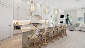 A modern kitchen with white cabinetry, a marble island, and wicker bar stools. - It's About Time|Unobstructed Gulf Views|Private Pool|Gated Community (Seacrest)