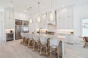 A modern kitchen with white cabinetry, a central island, and a seating area with wicker chairs.