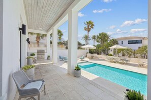 A covered outdoor area with a pool, seating, and a view of a house and palm trees.
