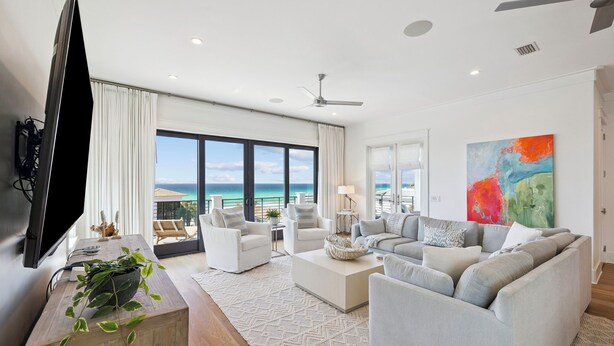 A modern living room with a large window, a flat-screen TV, and a ceiling fan. - It's About Time|Unobstructed Gulf Views|Private Pool|Gated Community (Seacrest)