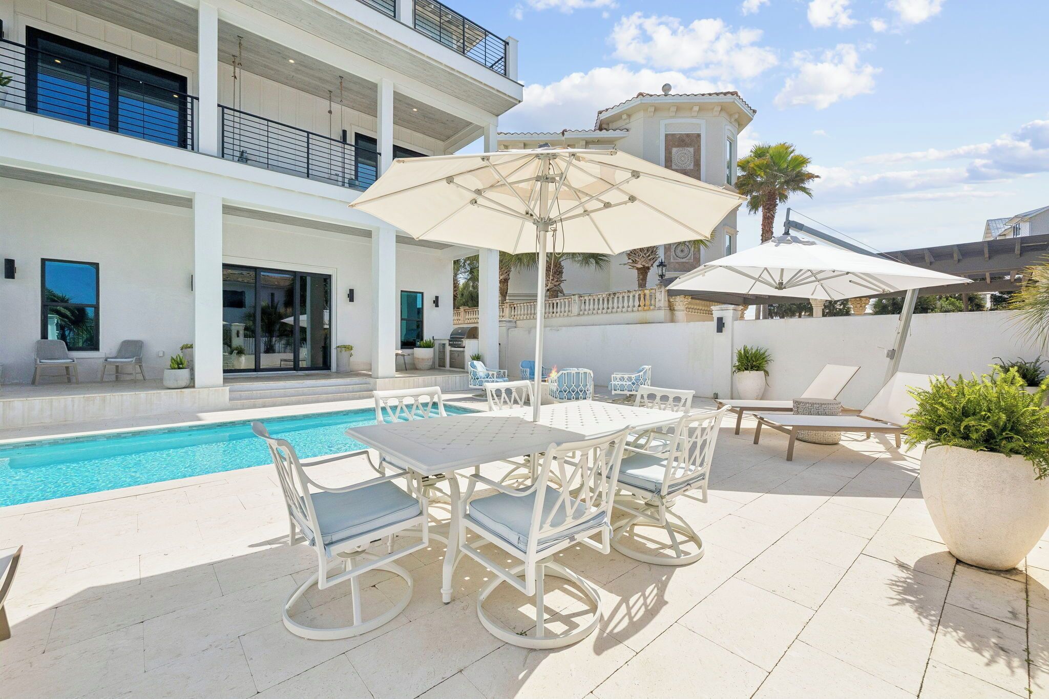 Un espace aménagé au bord de la piscine, avec une table et des chaises, un grand parasol et une vue sur un immeuble doté de balcons.