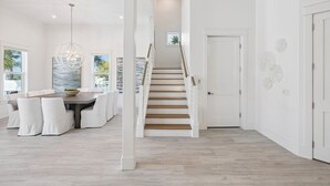 A spacious room with a dining area, a staircase, and a door leading to another room. - It's About Time|Unobstructed Gulf Views|Private Pool|Gated Community (Seacrest)