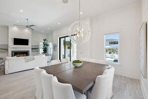 A modern living room with a fireplace, white furniture, a dining table, and a large window with a view.
