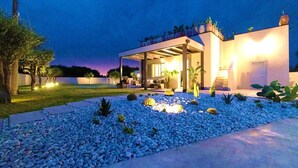 A modern house with a covered outdoor area, a garden with blue pebbles, and a well-lit entrance. - Villa Olive & Champagne con piscina privata (Santa Maria del Focallo)