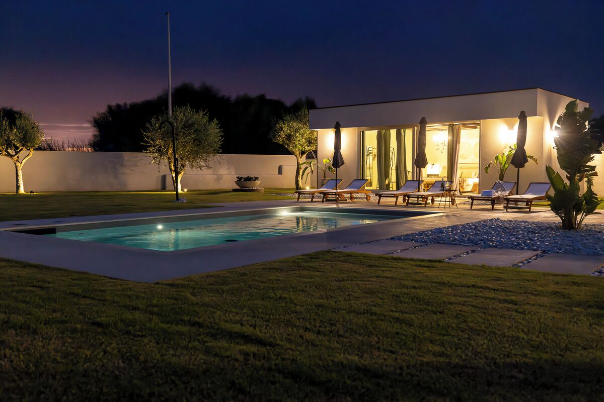 A modern house with a swimming pool, lounge chairs, and a well-lit patio area.