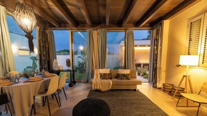 A modern dining area with a round table set for four, a sofa with cushions, and a black pouf. - Villa Olive & Champagne con piscina privata (Santa Maria del Focallo)