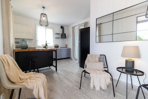A modern kitchen with a wooden island, a dining area with a chair and table, and a living area with a sofa and a lamp. - Villa Olive & Champagne con piscina privata (Santa Maria del Focallo)