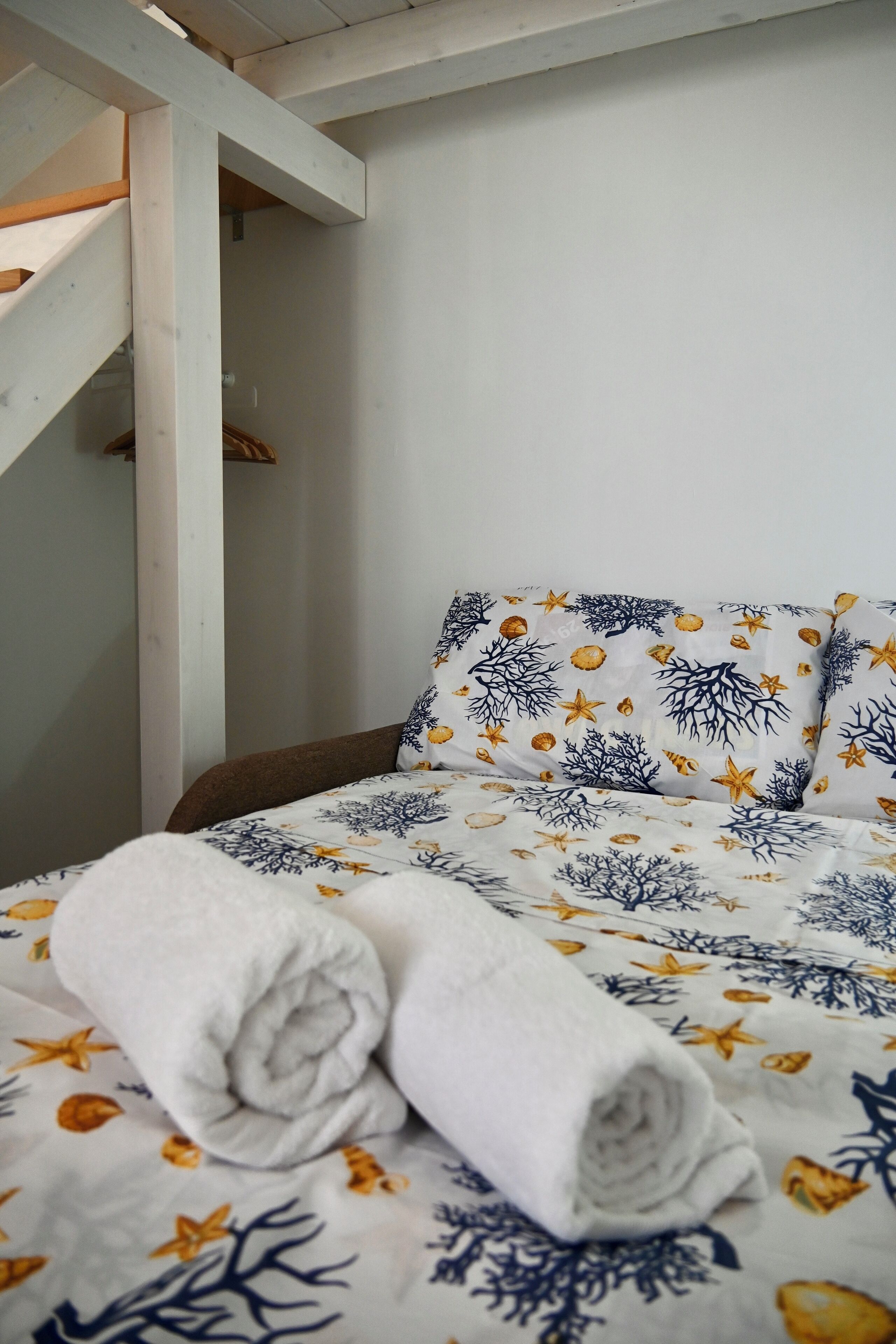 A bed with a white and blue patterned bedspread, a rolled white towel, and a wooden headboard.