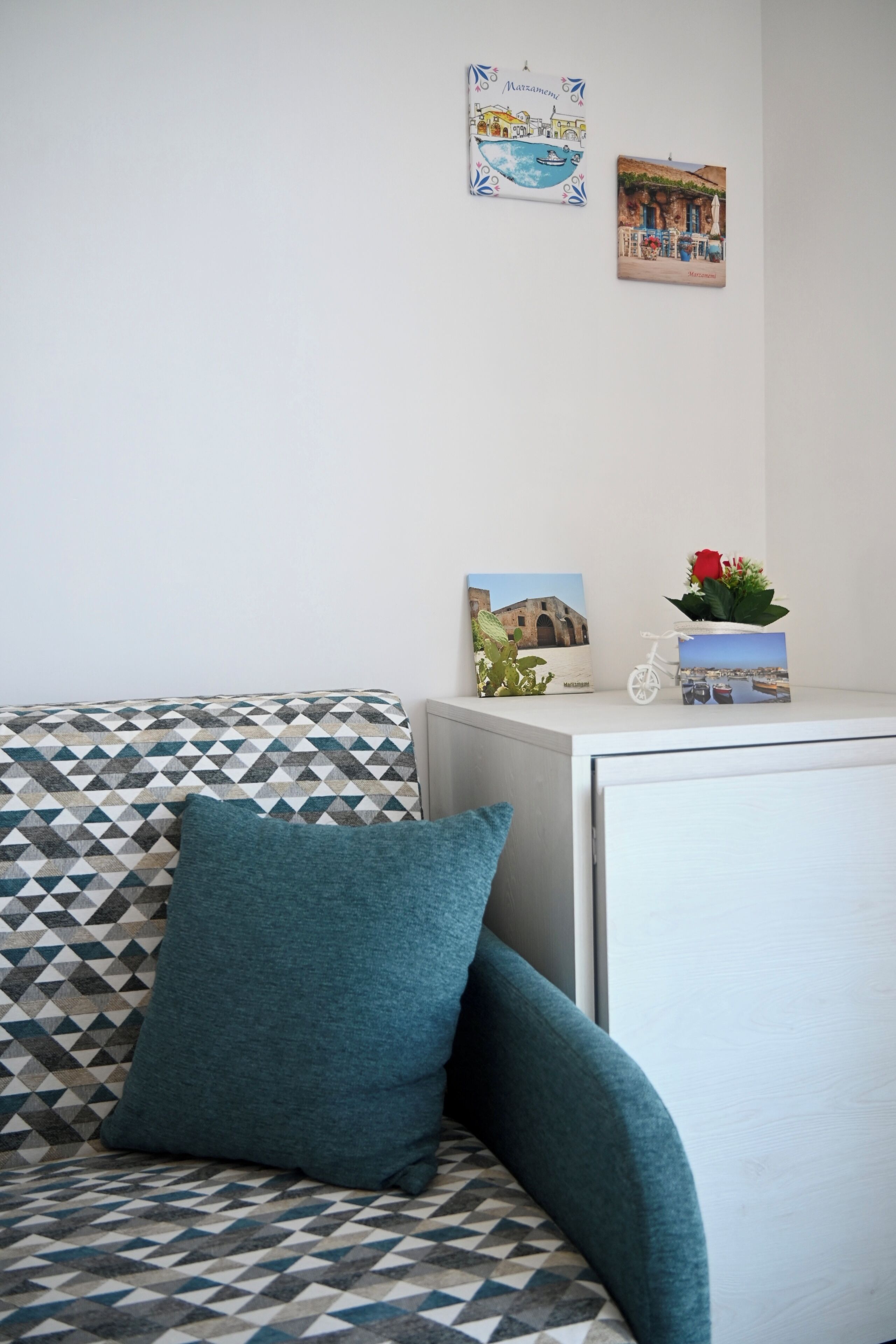 Ein Zimmer mit einer gemusterten Couch, einem kleinen weißen Schrank und zwei gerahmten Bildern an der Wand.