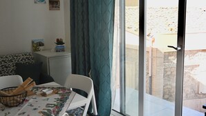 Ένα δωμάτιο με τραπέζι και καρέκλες για φαγητό, ένα μικρό ντουλάπι, μια κουρτίνα και μια συρόμενη γυάλινη πόρτα που οδηγεί σε έναν εξωτερικό χώρο.