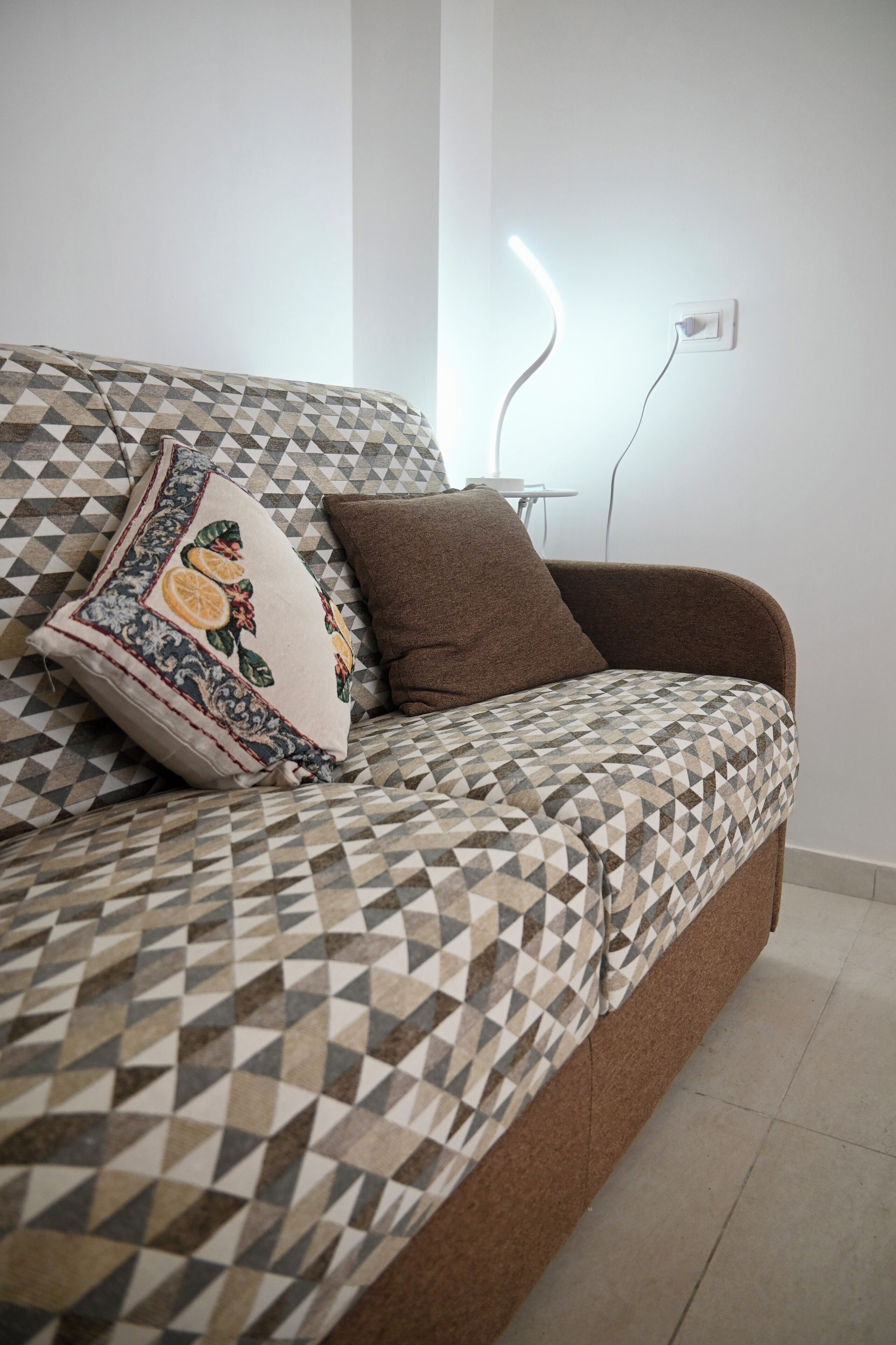 Un sofá con funda de estampado geométrico, un cojín marrón y un almohadón decorativo con motivos de frutas.