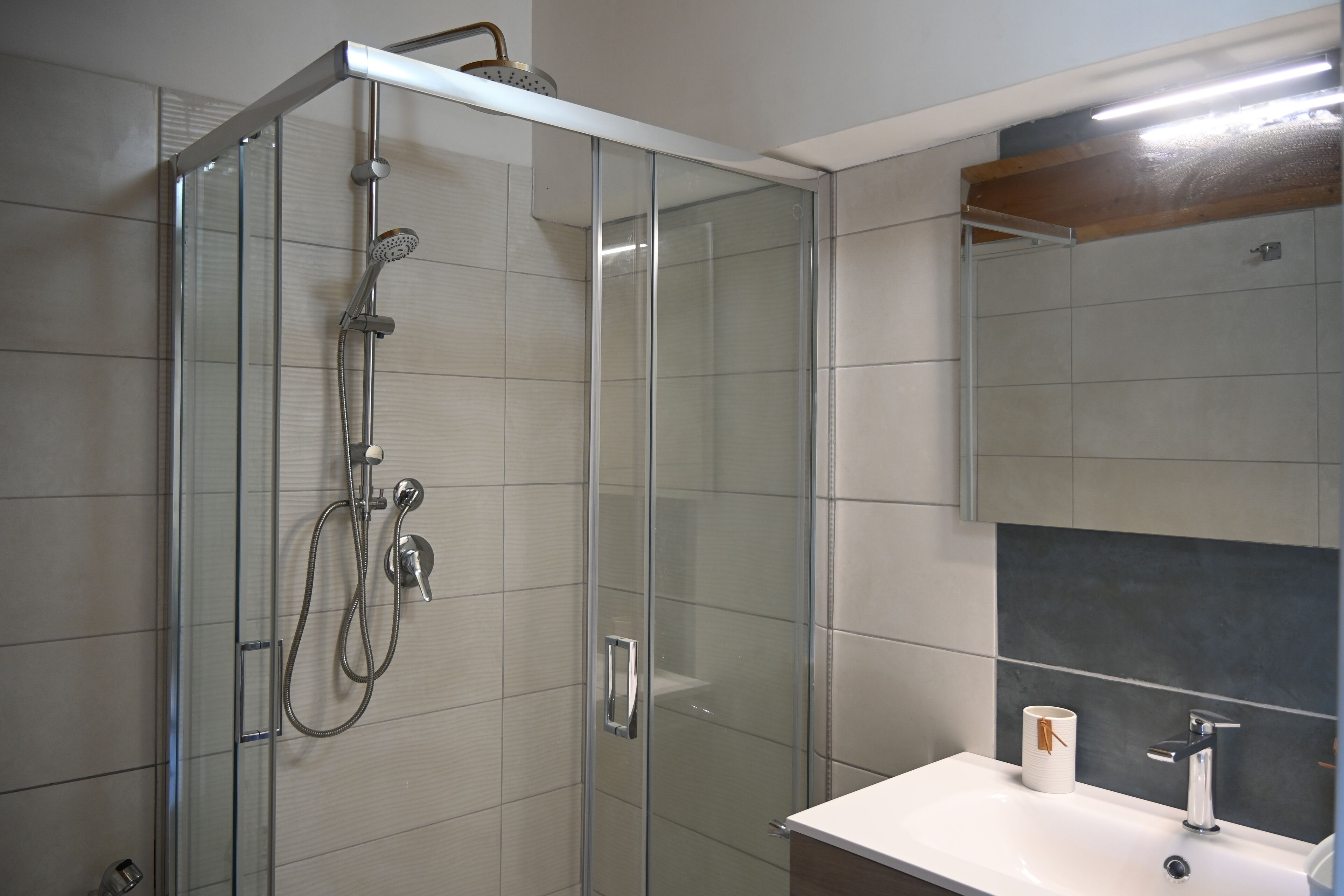 Un baño moderno con ducha envuelta en cristal, un lavabo blanco y un espejo sobre él.