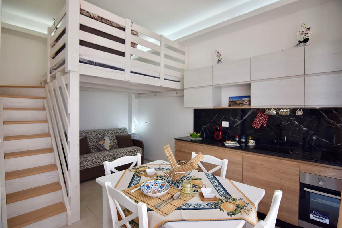 Eine moderne Küche mit Essbereich, ausgestattet mit einer Holztreppe, weißen Möbeln und einer schwarzen Marmor-Spritzschutzwand.