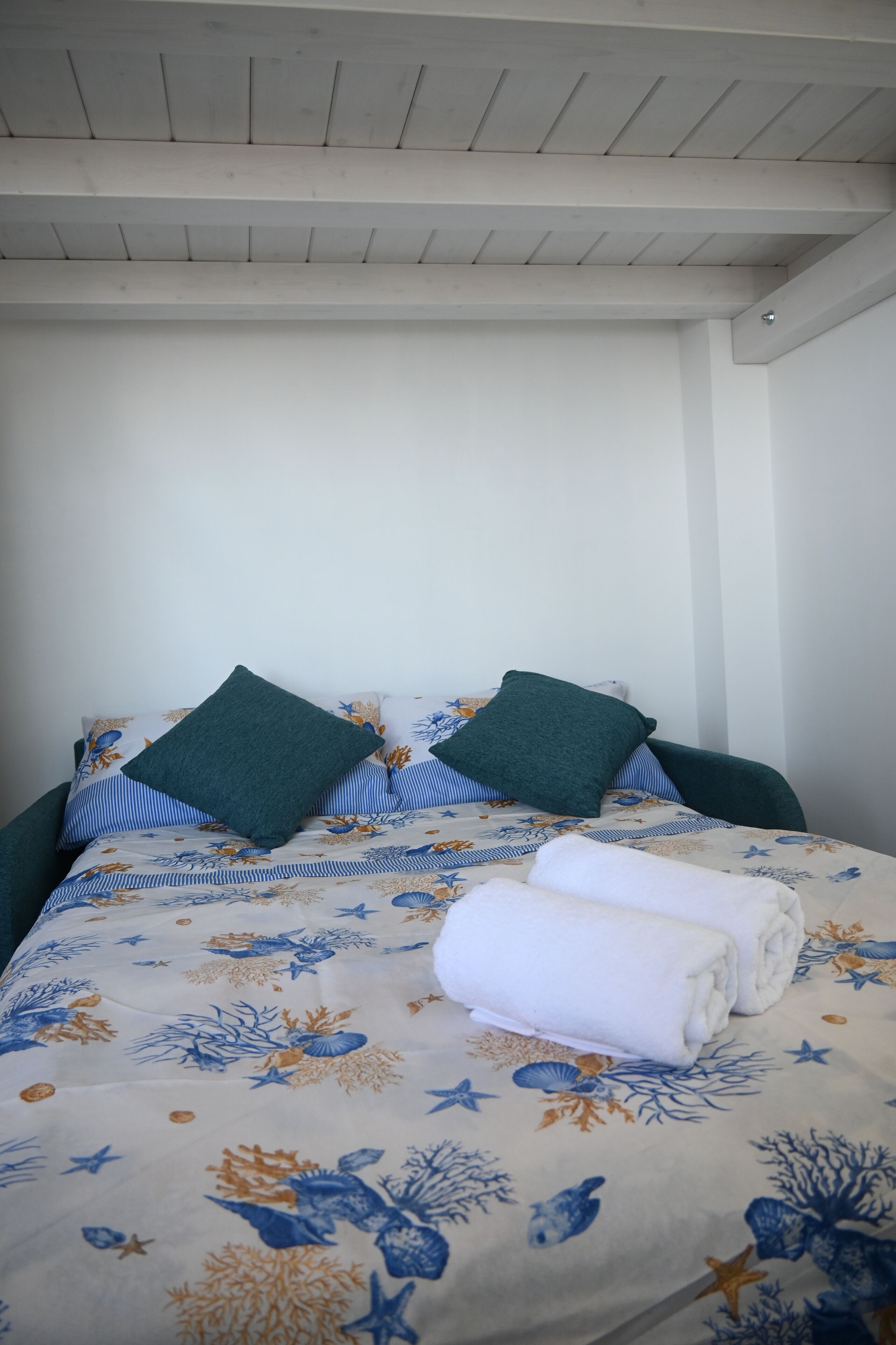 A bed with a floral bedspread, two green pillows, and two folded white towels.