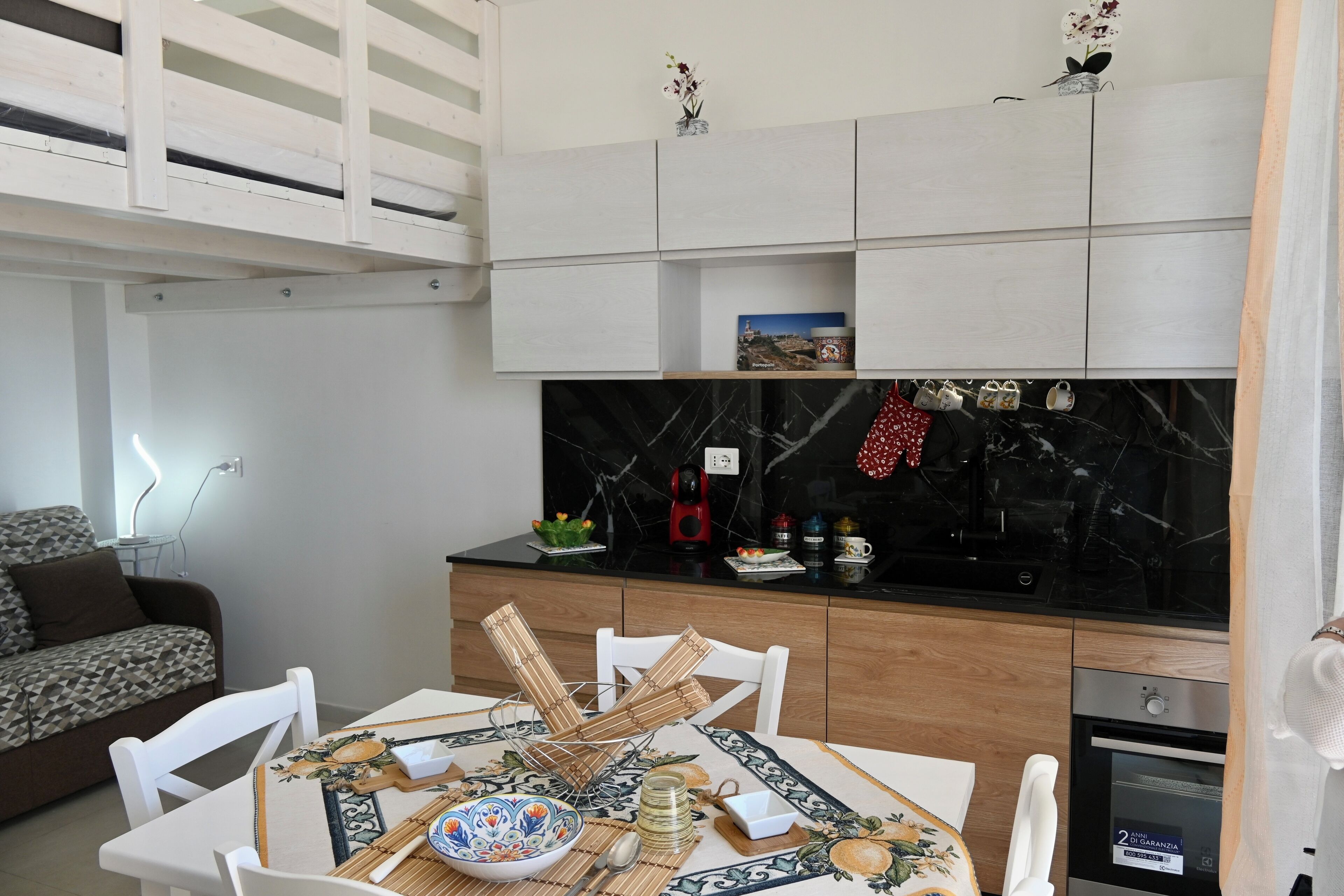 Een kleine keuken met een zwarte marmeren achterwand, een eettafel gedekt met borden en bestek, en een witte bank op de achtergrond.
