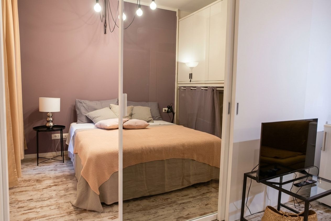 A bedroom with a bed, bedside lamp, TV on a stand, and a wardrobe.