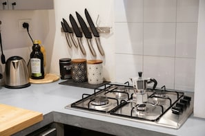 A kitchen with a gas stove, a kettle, a bottle of olive oil, and a set of knives on the wall. - Navigli Urban Suite (Milano)