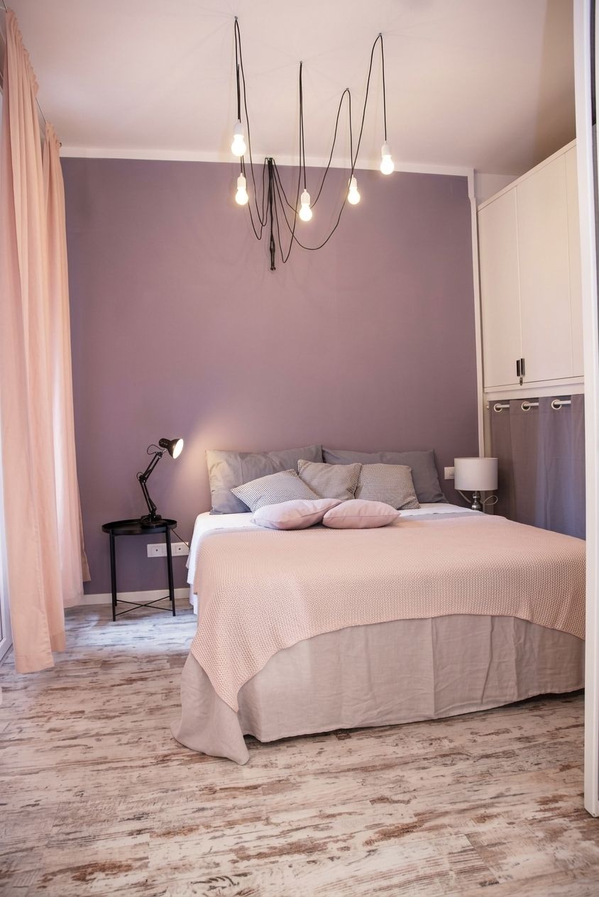 A bedroom with a bed, bedside lamp, and a hanging light fixture.
