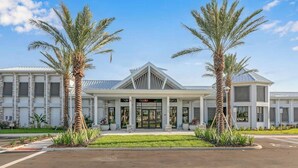 A modern building with a central entrance, flanked by palm trees, and a parking lot in front. - Modern Paradise at Windsor Cay, pool and Game Room (Clermont)