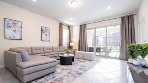 A modern living room with a grey sectional sofa, a round coffee table, and a large window with curtains. - Modern Paradise at Windsor Cay, pool and Game Room (Clermont)
