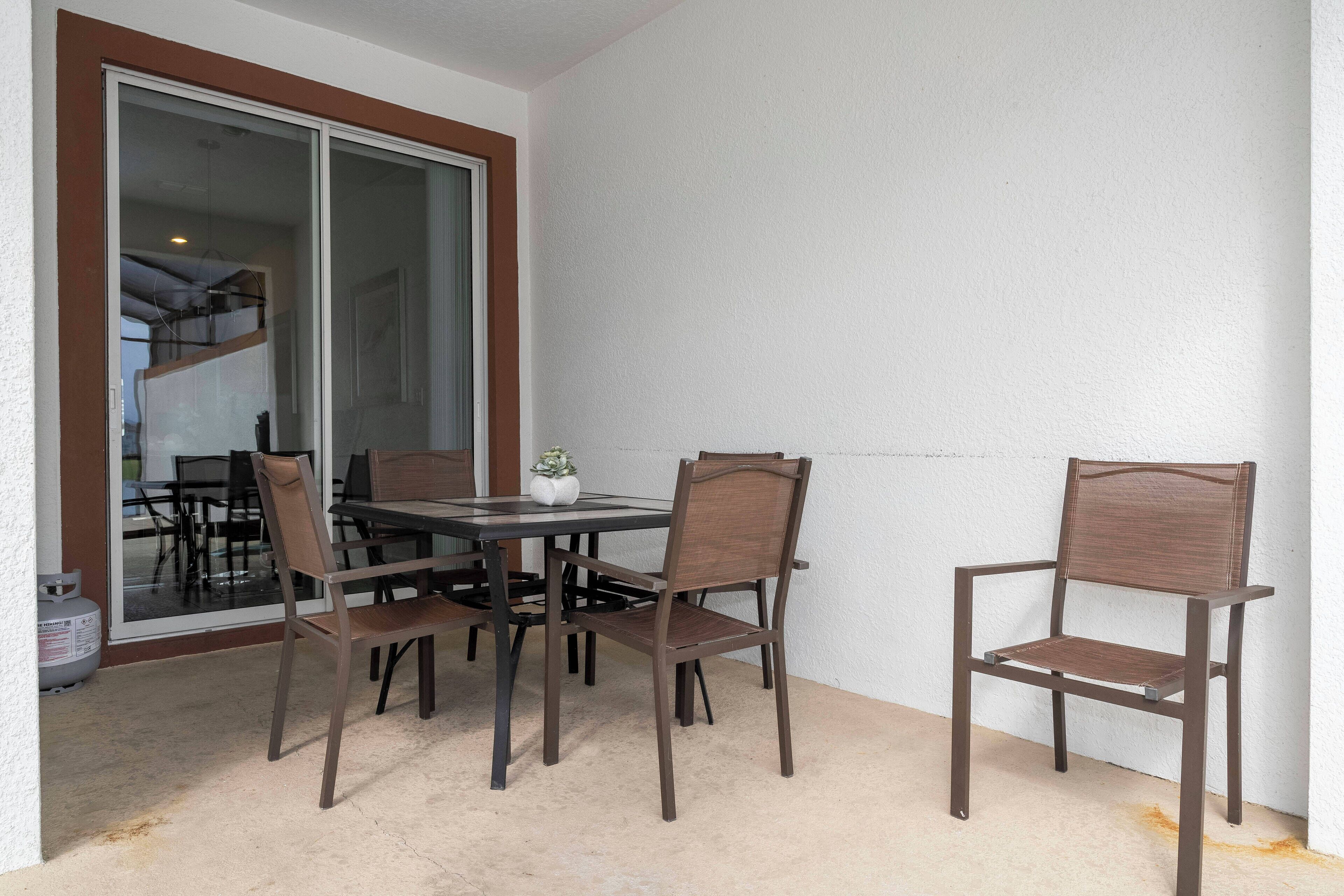 Un espace repas comprenant une table et quatre chaises, une porte-fenêtre coulissante et un sol en béton.