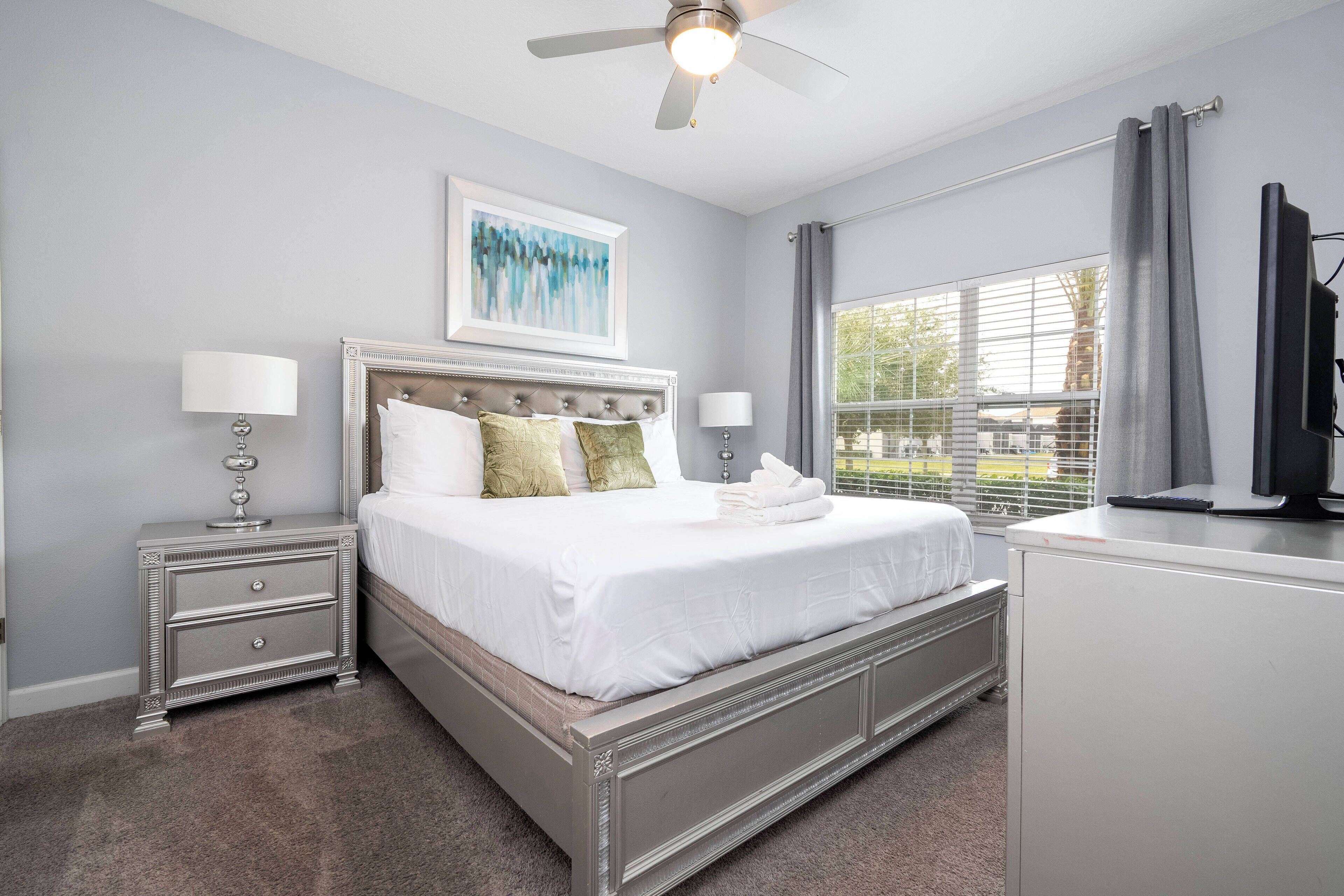 A bedroom with a bed, nightstands, a ceiling fan, a window with curtains, and a TV.