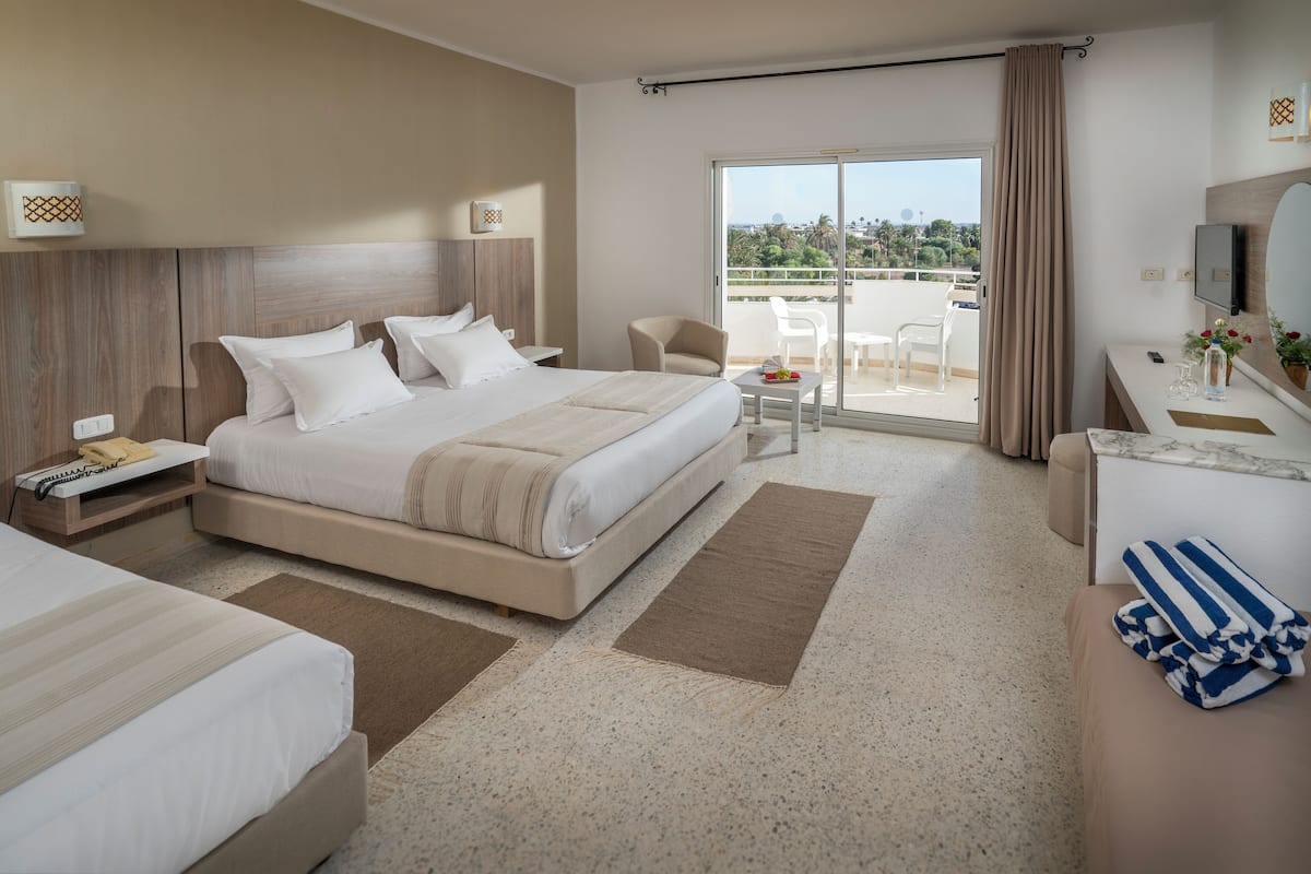 A hotel room with a large bed, a desk, a chair, and a balcony with a view.