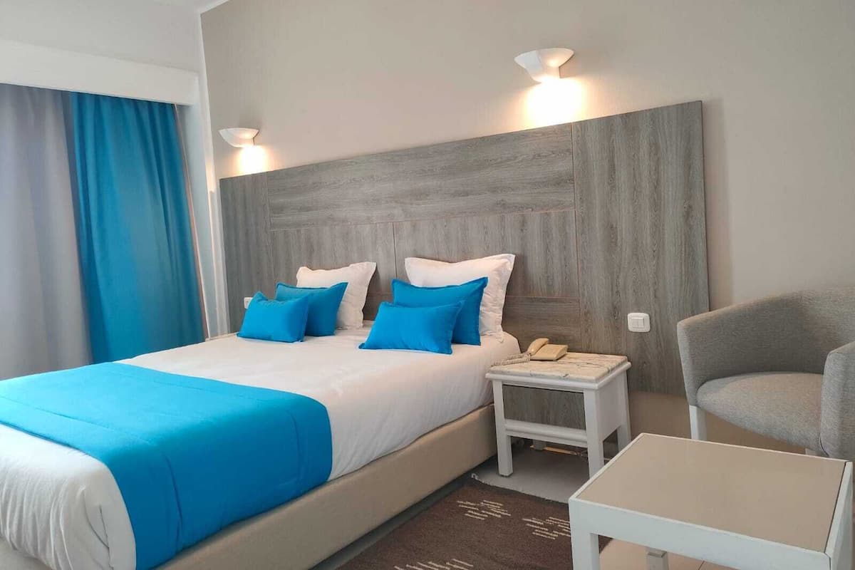 A hotel room with a bed, a nightstand, a chair, and a small table.
